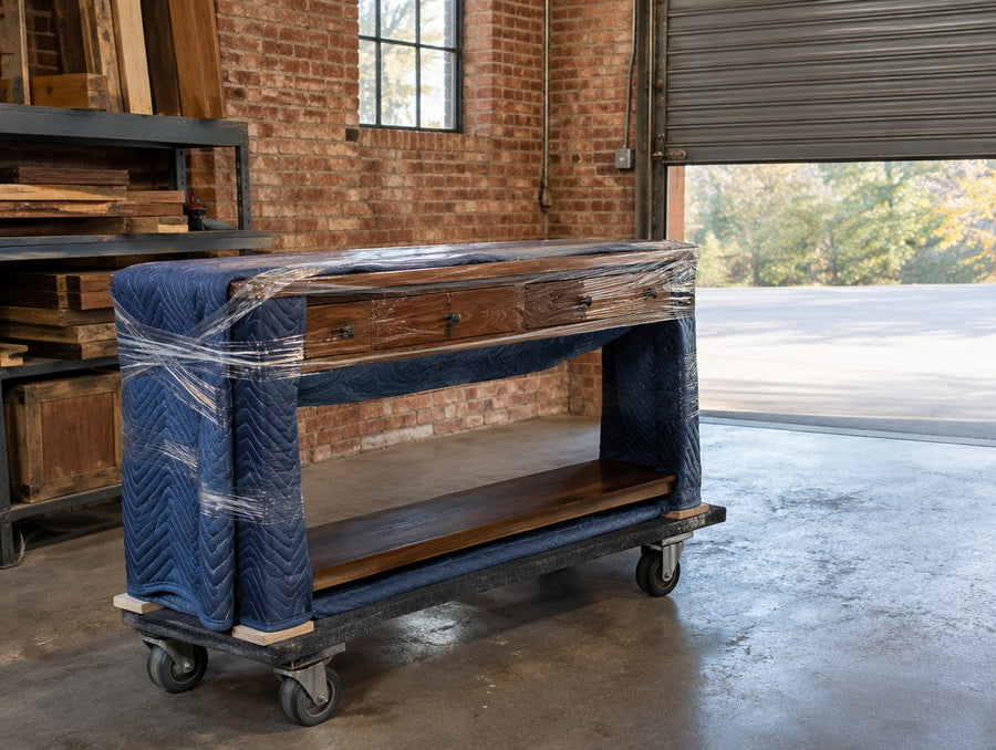 A finished solid wood console wrapped for delivery by the shop's roll-up door